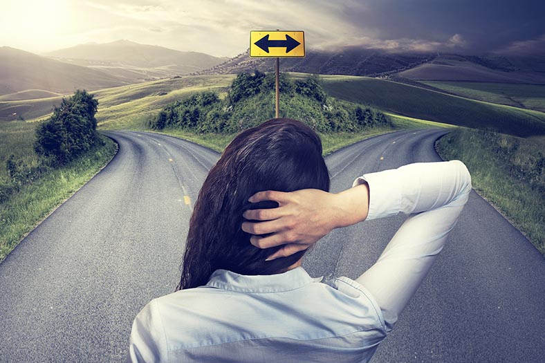Image of person at a crosing point in the road. She doesn't know if she should go left or right.